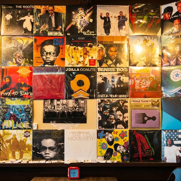 A wall covered with a vibrant collage of hip-hop and R&B vinyl record album covers.