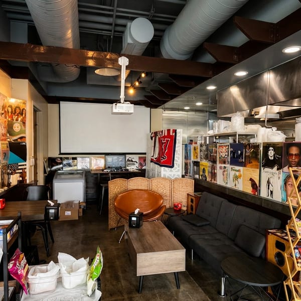 Eclectic restaurant interior with vinyl records on walls, a projector screen, and a casual seating area.