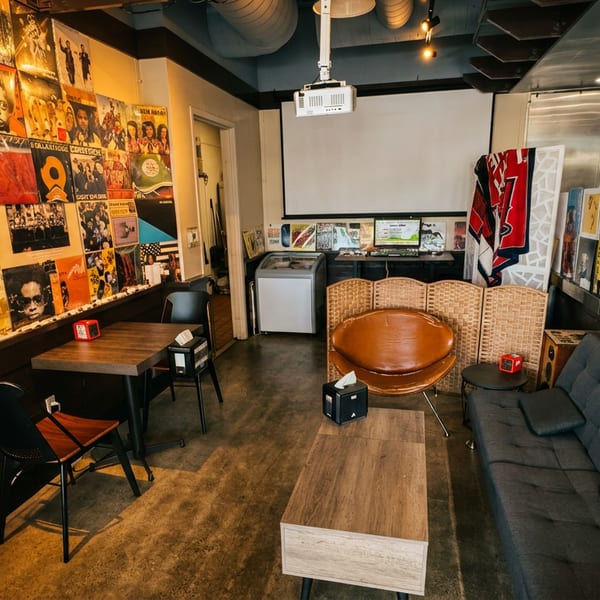 Cozy restaurant interior with vinyl record-covered walls, a projector screen, and various seating arrangements.