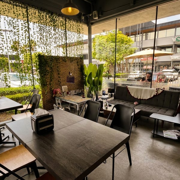 Modern cafe interior with dark tables, sofas, and large windows overlooking a parking lot and shops.